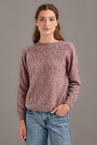 Woman wearing a heather and mocha patterned sweater and blue jeans against a gray background