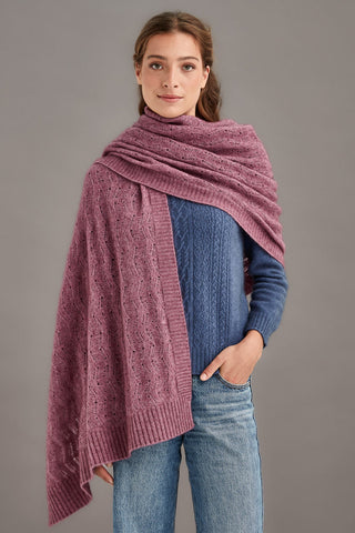 Woman wearing a heather pink knitted shawl over a blue sweater against a gray background