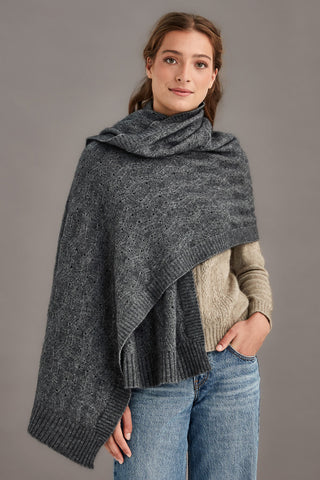 Woman wearing a pewter gray knitted shawl over a brown sweater against a gray background