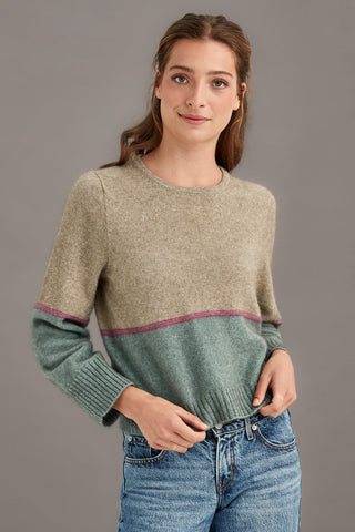Woman wearing a colourblocked sweater with green and beige colors on a gray background