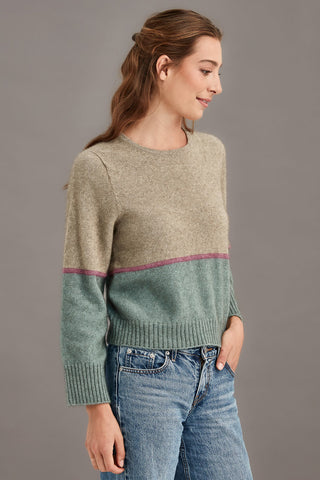 Woman wearing a colourblocked sweater with green and beige colors on a gray background