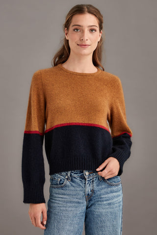 Woman wearing a colourblocked sweater with a brown top and black bottom with a red stripe paired with blue jeans against a gray background.