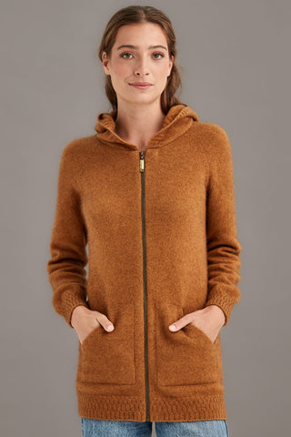 Woman wearing a honey brown hooded knit jacket against a gray background