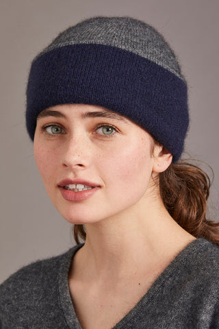 Woman wearing a navy and pewter knitted hat and cardigan against a gray background