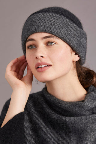 Woman wearing a pewter and charcoal gray knitted hat and cardigan against a gray background
