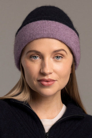 Woman wearing a lilac and navy knitted hat and cardigan against a gray background