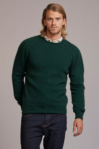 Man wearing a green sweater and dark pants against a plain background