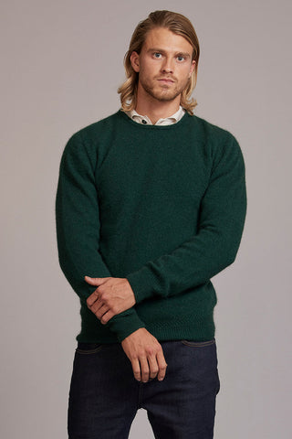 Man wearing a green sweater over a collared shirt against a gray background