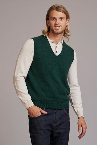 Man wearing a green sweater vest over a white shirt on a gray background