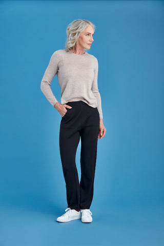 Woman wearing a light gray sweater and black merino pants against a blue background