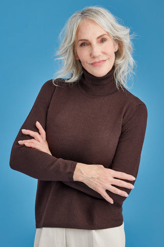Woman wearing a brown polo turtleneck sweater against a blue background