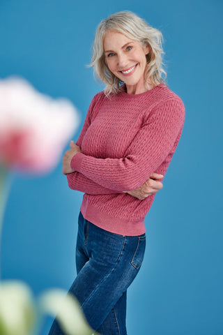 Woman wearing a pink merino sweater and blue jeans against a blue background