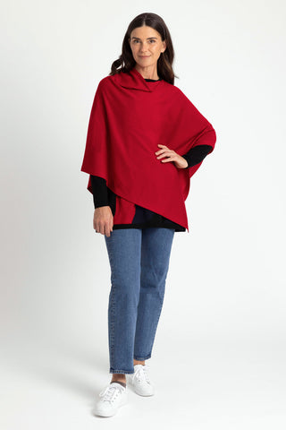 A woman wearing a red asymmetric poncho with blue jeans