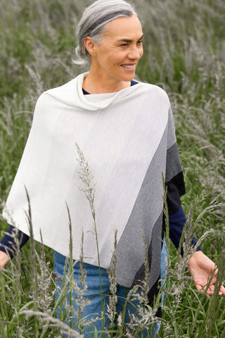 A woman standing in a field with a graduated stripe poncho featuring ombre stripes in black and gray, draped over her shoulders.