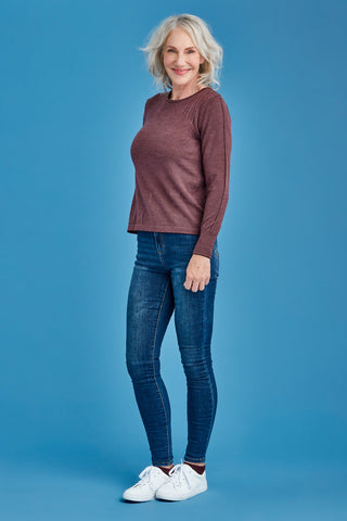 Woman wearing a mauve sweater, blue jeans, and white sneakers on a blue background