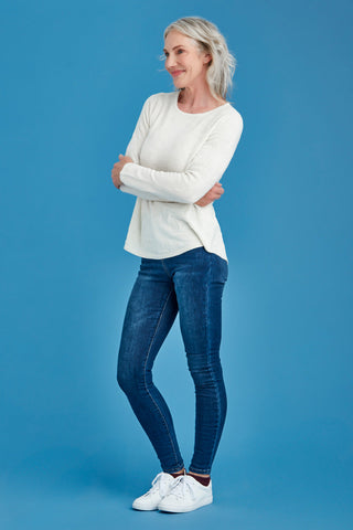 Woman wearing a white sweater and blue jeans against a blue background