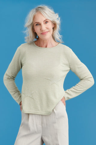 Woman wearing a light green striped merino sweater and blue jeans against a blue background