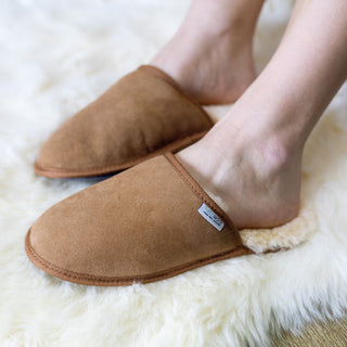 Pair of brown scuff slippers with white sheepskin lining on a sheepskin rug